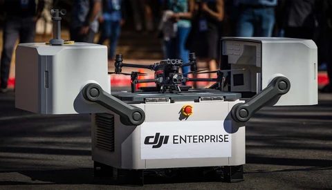 DJI Enterprise drone system displayed on white case with dual articulated arms and red battery modules.