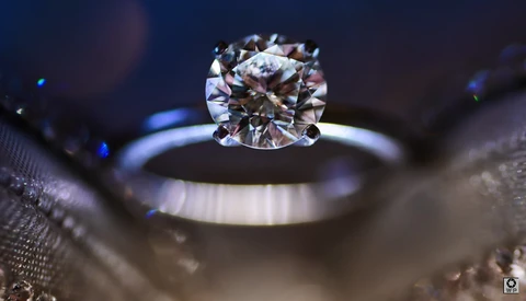 Diamond solitaire engagement ring with cushion cut stone photographed macro with shallow depth of field against dark background.