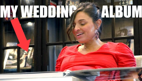 Woman in red shirt viewing wedding album pages in display case with shelving behind.