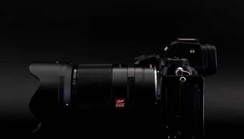 Professional camera with telephoto lens mounted, positioned against a dark background with dramatic side lighting.
