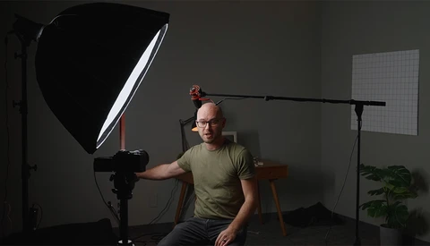 Photographer demonstrating studio lighting setup with softbox and boom arm positioned over subject.