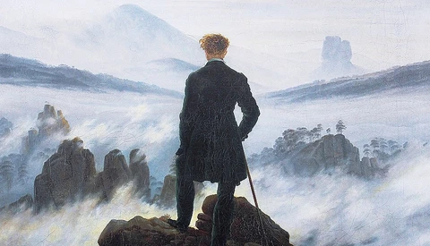 Man in dark coat standing on rocky outcrop overlooking misty mountain valley.