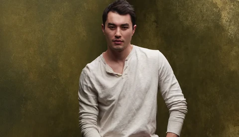 Man wearing cream long-sleeve henley shirt against textured olive-green background.