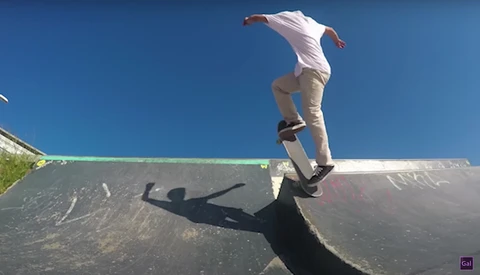 Skateboarder performing a trick on a ramp with clear blue sky above and dramatic shadow cast on the ramp surface.