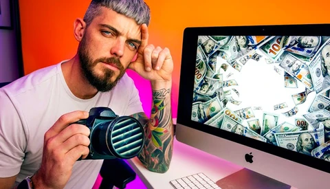 Photographer holding a mirrorless camera while looking at a desktop monitor displaying dollar bills..