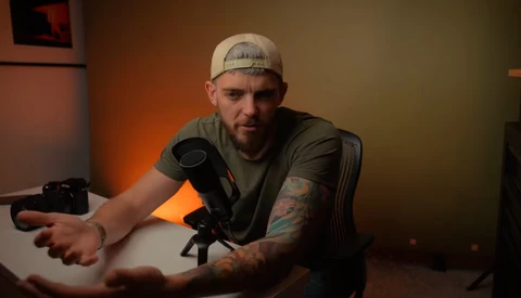 Male content creator seated at desk with studio microphone and warm orange lighting setup.