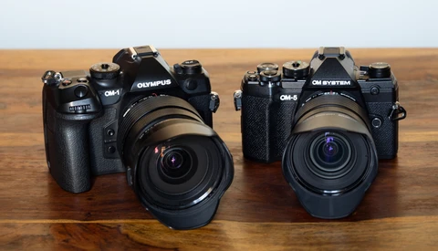 Two Olympus OM-series film cameras with attached lenses displayed on a wooden surface.