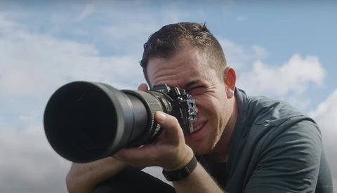 Male photographer shooting with a telephoto lens against a cloudy sky backdrop.