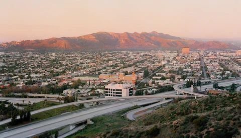 Sprawling desert city at sunset with mountains in the background and multiple highway interchanges in the foreground.