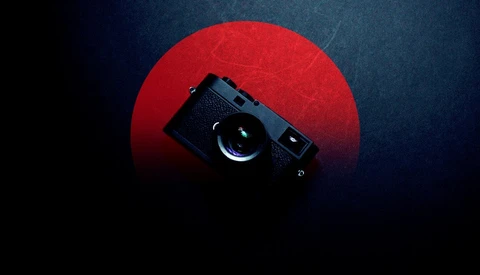 Black rangefinder camera positioned against a large red circular backdrop on dark blue background.
