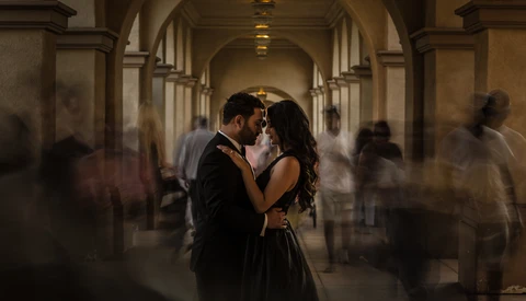 Couple kissing in an arched stone corridor surrounded by motion-blurred figures.