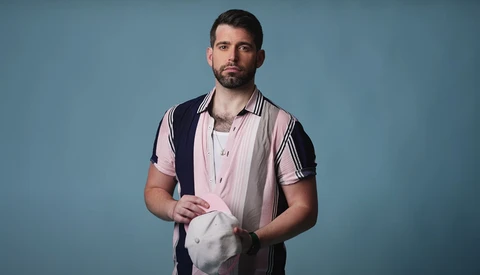 Man in pink and black striped shirt holding white fabric against blue background.