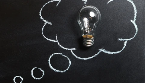 Incandescent light bulb centered in chalk-drawn cloud shapes on dark chalkboard surface.