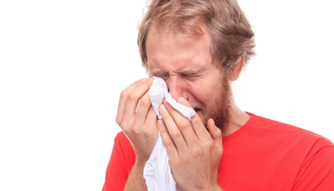 Man in red shirt holding tissue to his nose while sneezing or blowing his nose.
