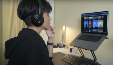 Person wearing headphones at desk viewing streaming interface on laptop screen.