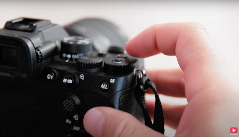 Photographer's hands adjusting camera controls on a professional DSLR body.
