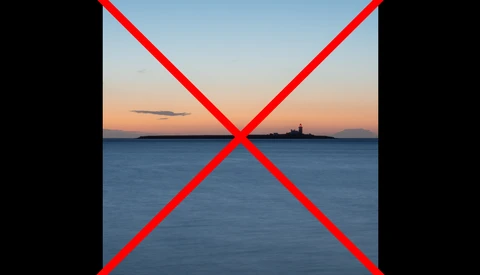Coastal seascape at dusk with silhouetted lighthouse on distant shore.