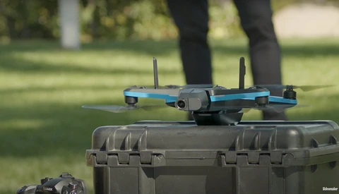 Blue and gray drone with extended arms and propellers positioned on a protective carrying case outdoors.