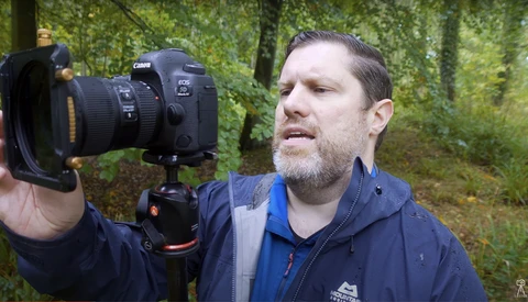 Photographer holding Canon EOS camera with wide-angle lens in forest setting.