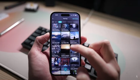 Hands holding a smartphone displaying a grid of thumbnail images and video content.