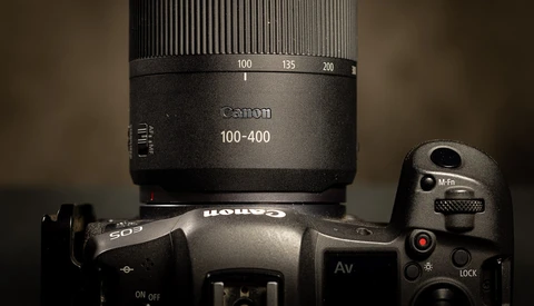 Canon EOS camera body with 100-400mm telephoto lens mounted, shown against neutral studio background.