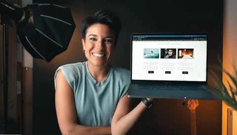 Creative professional smiling at camera while pointing to website portfolio displayed on monitor in studio setting.