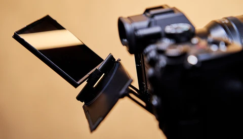 Camera flash diffuser attached to a DSLR camera against a warm beige background.