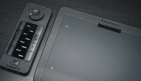 Drone remote controller with joystick and button panel displayed on dark surface next to tablet.