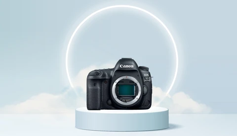 Canon EOS R5 mirrorless camera body displayed on a light blue cylindrical pedestal against a minimalist backdrop with a glowing circular neon ring.