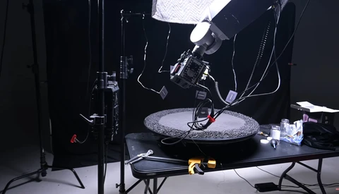 Professional overhead lighting setup with softbox and key light positioned above a circular reflective surface on a dark studio table.