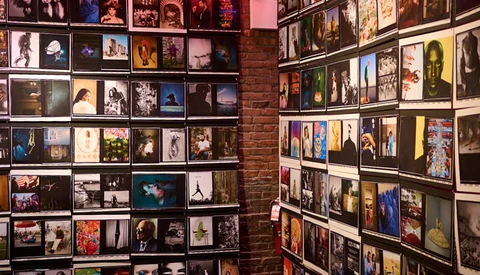 Gallery wall displaying hundreds of framed photographs and artwork arranged in a grid pattern across exposed brick.