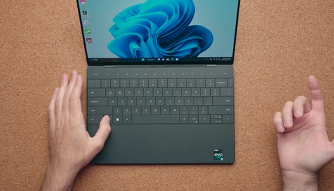 Hands positioning a laptop with Windows 11 startup screen on cork surface.