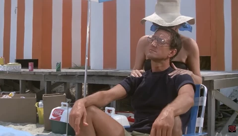 Two people sitting on a blue chair at a beach setup with striped backdrop and Coca-Cola branding visible.