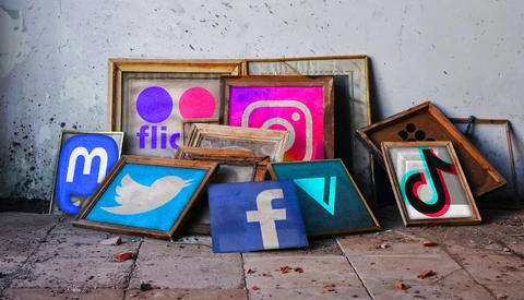 Social media platform logos displayed in wooden frames leaning against a weathered concrete wall.