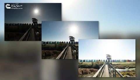 Wooden boardwalk stretching into a landscape with moored boats and fields under bright sunlight.