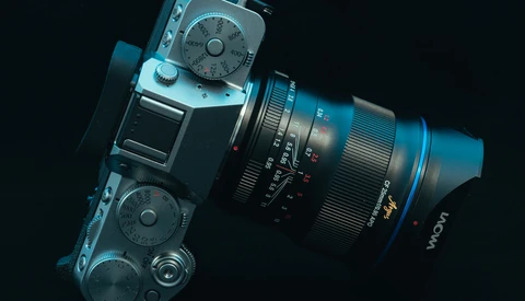 Blue mirrorless camera with attached zoom lens positioned diagonally against a black background.