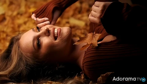 Woman lying on autumn leaves, looking upward with warm golden lighting.