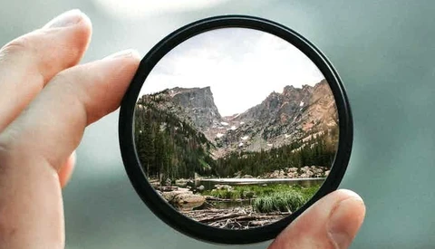 Mountain valley landscape framed through a circular lens filter held in hand.