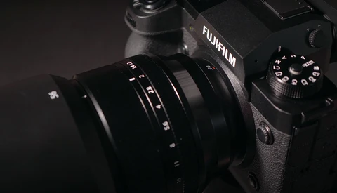 Fujifilm camera with attached lens against dark background, showing camera body and control dial.