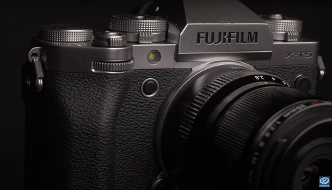 Fujifilm X-T5 camera with textured black body and attached lens, photographed against dark background.