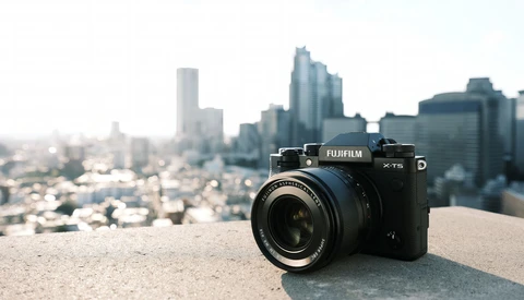 Fujifilm X-T5 camera on concrete ledge with blurred city skyline behind.