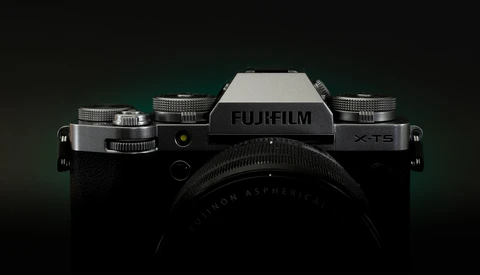 Fujifilm X-T5 mirrorless camera with mounted lens, shot against dark background with accent lighting.
