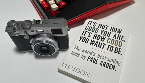 Rangefinder camera next to open book with motivational quote and red digital keyboard in background.