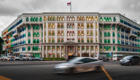 Colorful corner building with green and yellow-gold window frames and a flag on top, with blurred vehicles passing in foreground.