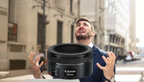 Man holding a Canon 50mm lens toward camera on an urban street.
