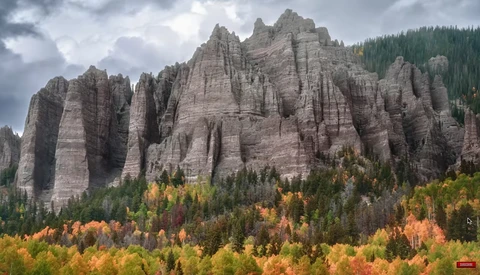Dramatic columnar rock formations rising above a forested valley in autumn.