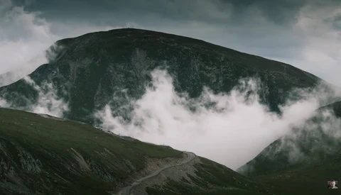 A verdant mountain peak shrouded in mist and low-hanging clouds beneath a dramatic overcast sky.