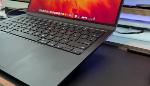 MacBook laptop displaying warm red and orange wallpaper with dock visible at screen top.