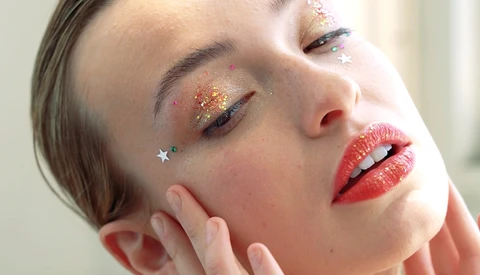 Close-up portrait of a woman with glittery eyeshadow and red lips, eyes closed.