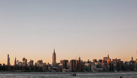 Manhattan skyline at golden hour with Empire State Building prominently lit in center.